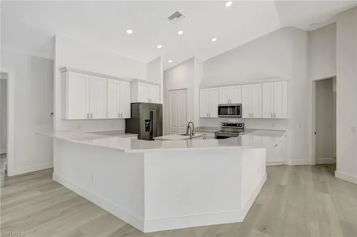 Kitchen featuring stainless steel appliances, baseboards, high vaulted ceiling, white cabinetry, and light wood-style floors