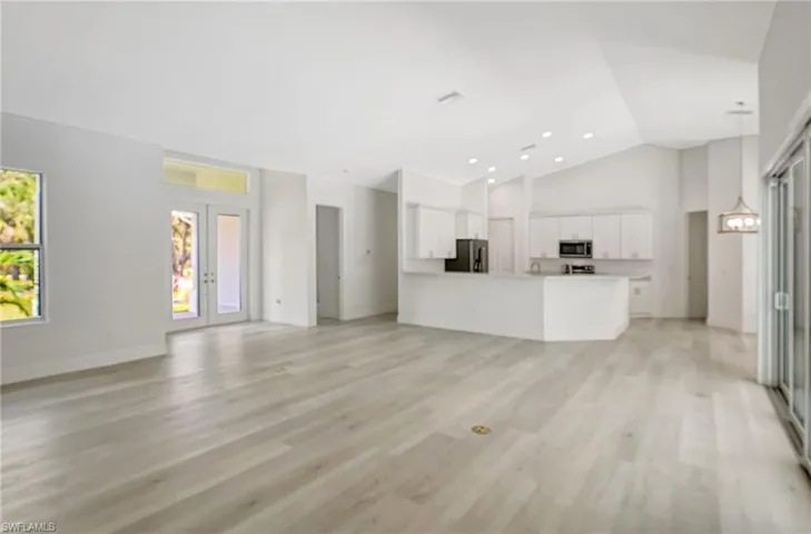 Unfurnished living room featuring high vaulted ceiling, light wood-type flooring, baseboards, and recessed lighting