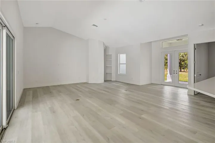 Unfurnished living room with french doors, vaulted ceiling, light wood-style floors, and baseboards
