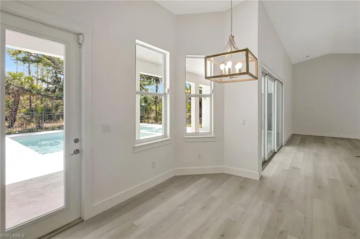 Unfurnished dining area featuring a chandelier, light wood-style flooring, lofted ceiling, and baseboards