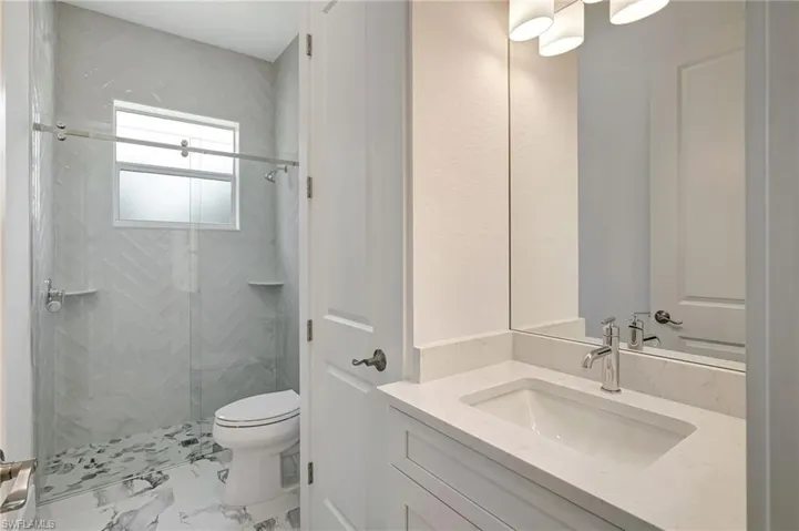 Bathroom with toilet, a stall shower, marble look tiles, and vanity