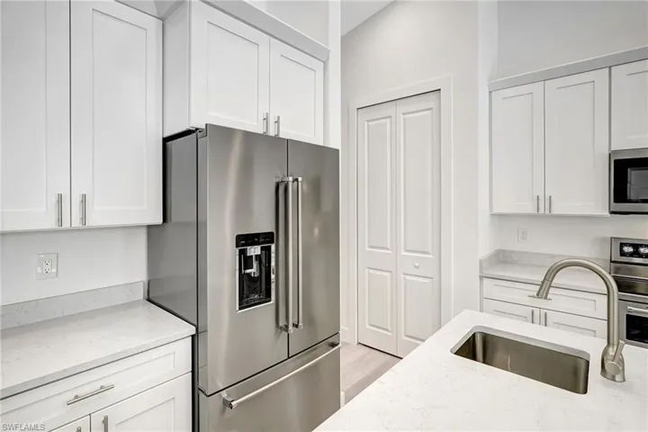 Kitchen featuring stainless steel appliances, a sink, white cabinetry, and light stone counters