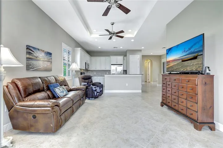 Living room with arched walkways, a ceiling fan, a tray ceiling, recessed lighting, and light tile patterned flooring