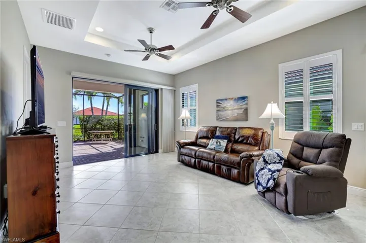 Living room with a ceiling fan, a raised ceiling, light tile patterned floors, and recessed lighting