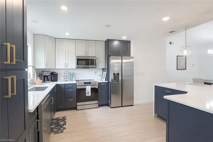 Kitchen with appliances with stainless steel finishes, hanging light fixtures, light stone countertops, light wood-style flooring, and recessed lighting