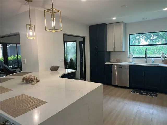 Kitchen with hanging light fixtures, stainless steel dishwasher, tasteful backsplash, light stone counters, and dark cabinetry