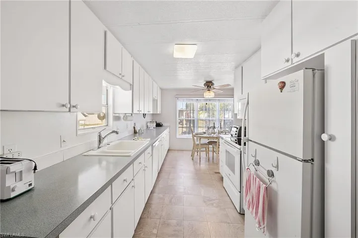 Kitchen featuring white cabinets, white appliances, ceiling fan, a textured ceiling, and dark countertops