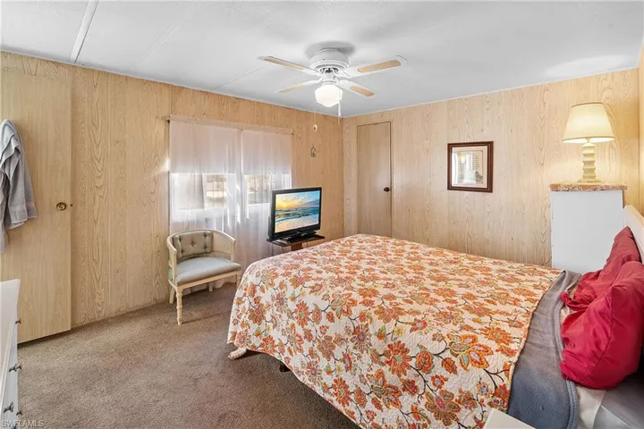 Carpeted bedroom featuring wood walls and a ceiling fan