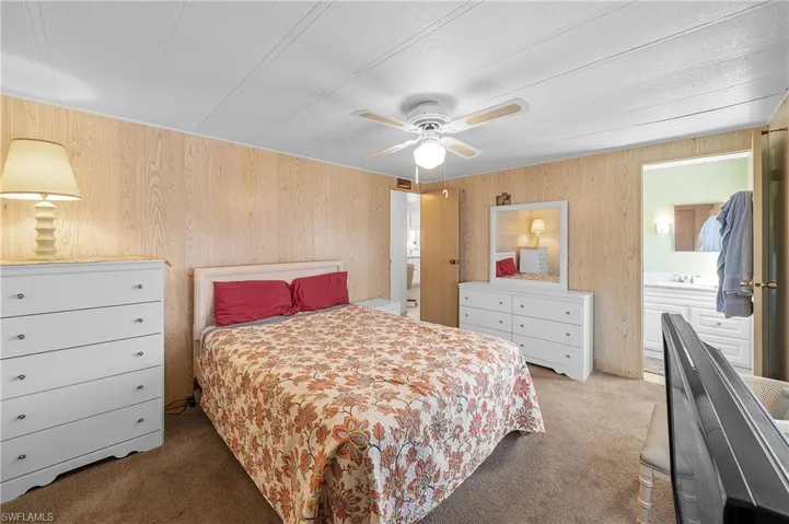 Bedroom featuring ensuite bathroom, carpet floors, wood walls, and a ceiling fan