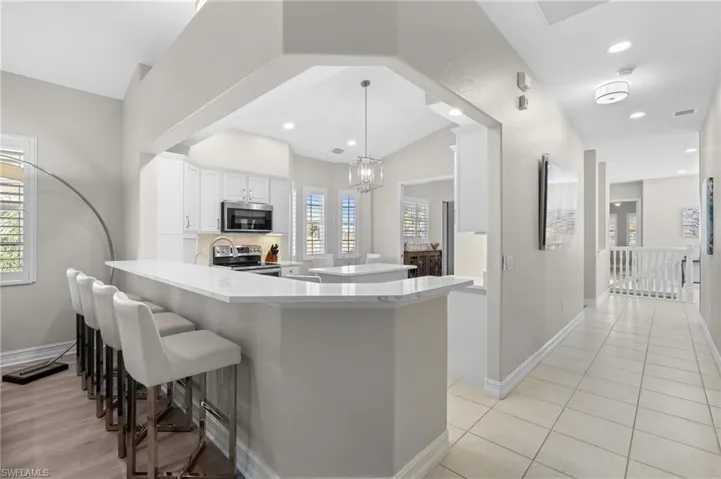 Kitchen featuring a kitchen breakfast bar, an inviting chandelier, a peninsula, white cabinetry, and appliances with stainless steel finishes