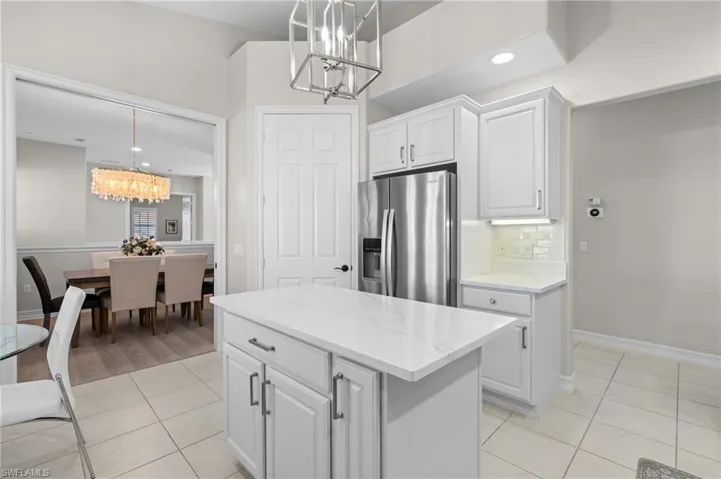 Kitchen featuring white cabinets, stainless steel refrigerator with ice dispenser, a chandelier, pendant lighting, and light tile patterned flooring