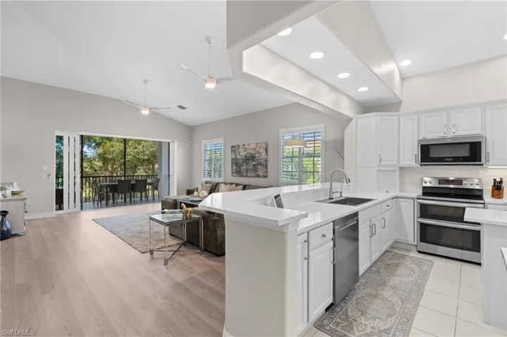 Kitchen featuring a sink, open floor plan, light countertops, appliances with stainless steel finishes, and white cabinetry