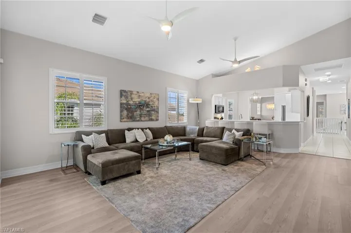 Living room featuring visible vents, baseboards, ceiling fan, light wood-type flooring, and lofted ceiling