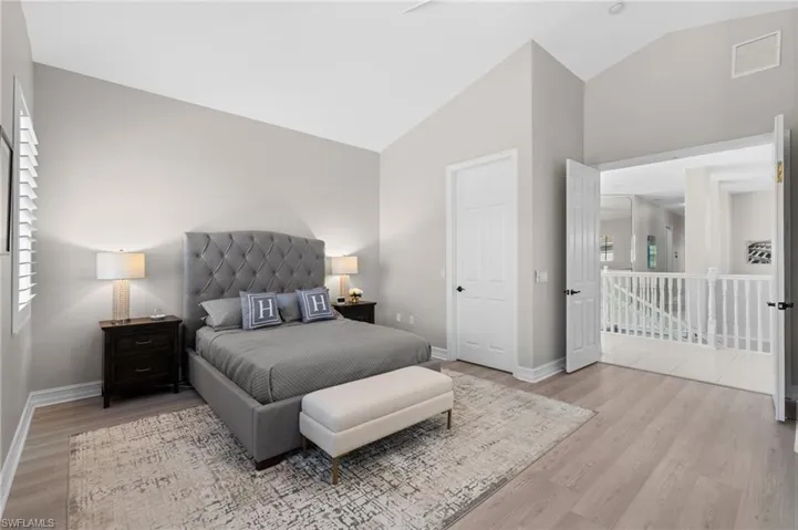 Bedroom with visible vents, baseboards, high vaulted ceiling, and wood finished floors