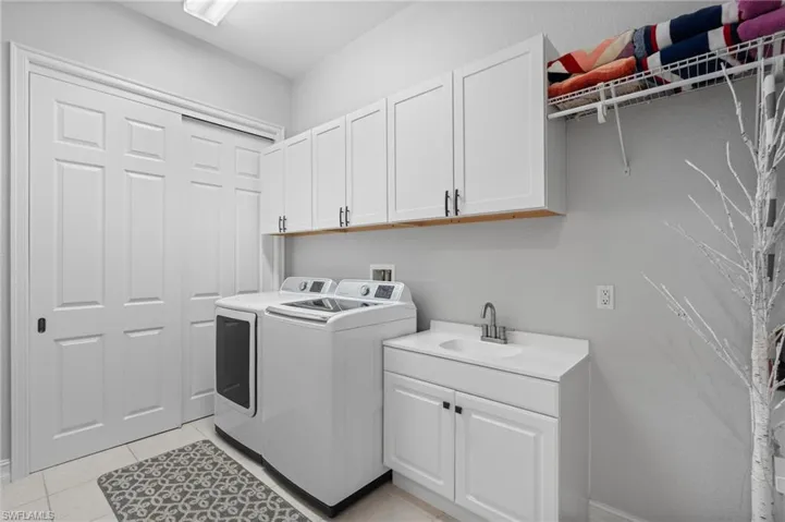 Laundry area with a sink, light tile patterned floors, cabinet space, and separate washer and dryer