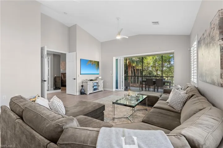 Living area featuring high vaulted ceiling, a ceiling fan, visible vents, wood finished floors, and baseboards