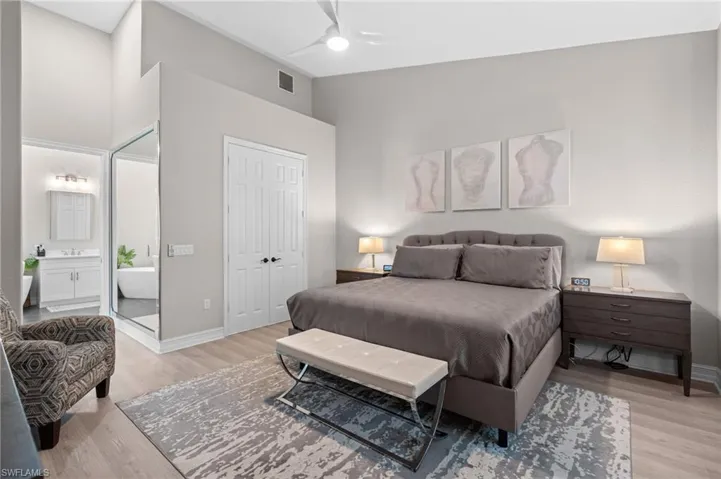 Bedroom featuring connected bathroom, light wood-style flooring, a towering ceiling, visible vents, and baseboards