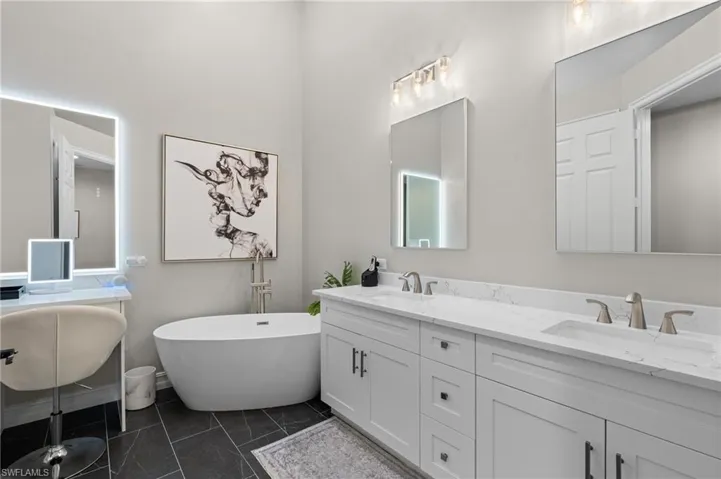 Full bath with double vanity, marble finish floor, a sink, and a soaking tub