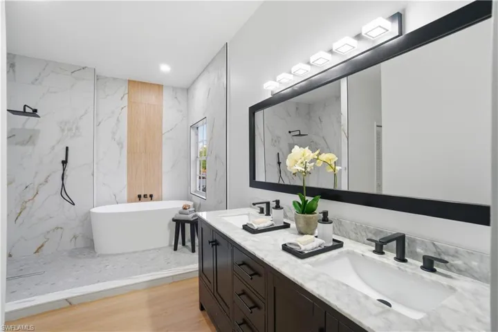 A beautifully redesigned primary wet room featuring marble-look porcelain tile, a sleek walk-in shower, freestanding soaking tub, double vanity with dark, shaker cabinets, with modern matte black fixtures, and abundant natural light