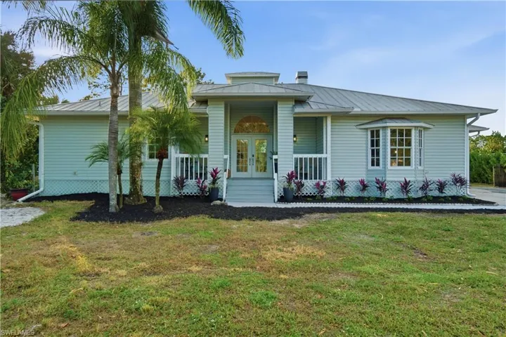 Elegant front approach highlighted by French doors, a covered porch, timeless metal roof and expansive lawn