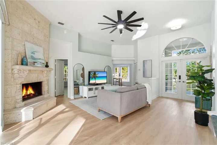 Sunlit living anchored by a striking travertine fireplace, highlighted by elegant glass French doors and an arched transom that fills the room with natural light