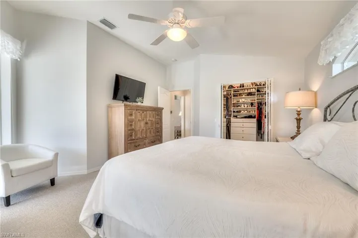 Carpeted bedroom featuring vaulted ceiling, a walk in closet, ceiling fan, and a closet