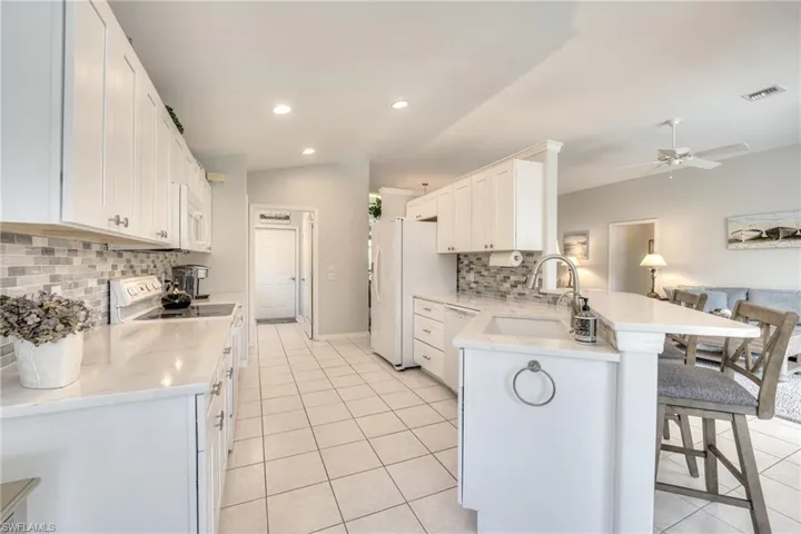 Kitchen with sink, a breakfast bar area, white cabinets, kitchen peninsula, and white appliances