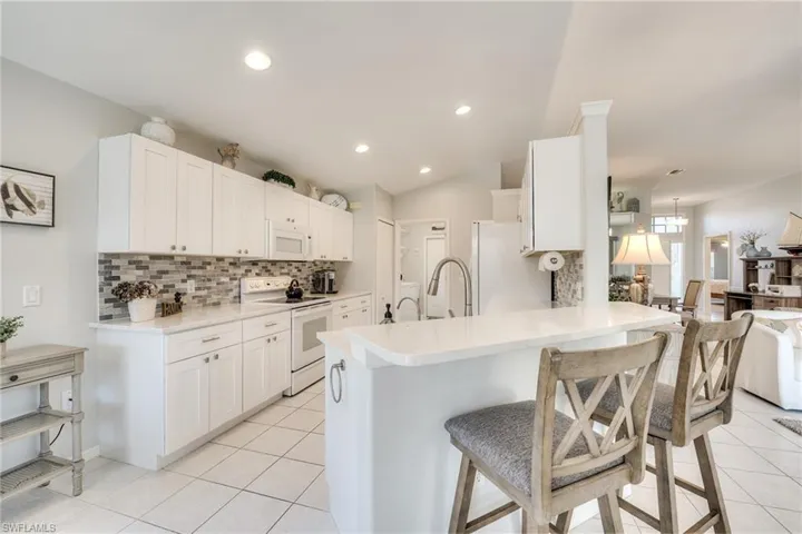 Kitchen with white cabinetry, white appliances, a breakfast bar, and kitchen peninsula