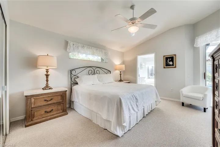 Carpeted bedroom with ceiling fan, ensuite bath, and vaulted ceiling