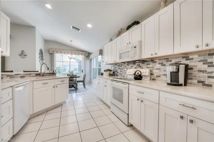 Kitchen featuring light tile patterned floors, white appliances, sink, white cabinets, and decorative light fixtures