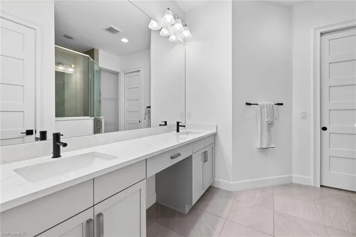 Primary bath with double vanity, a large shower, neutral tile and a spacious walk-in custom closet.