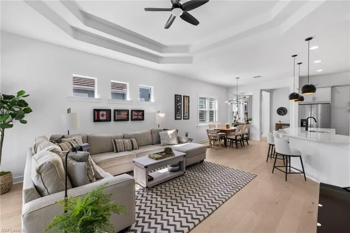 Living area featuring light wood-type flooring, a ceiling fan, a raised ceiling, and hanging lights
