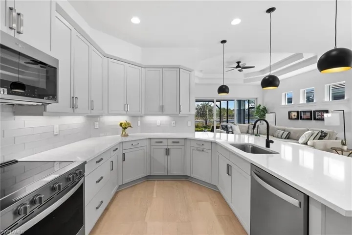 Kitchen with stainless steel appliances, light wood-style floors, open floor plan, ceiling fan, and hanging light fixtures