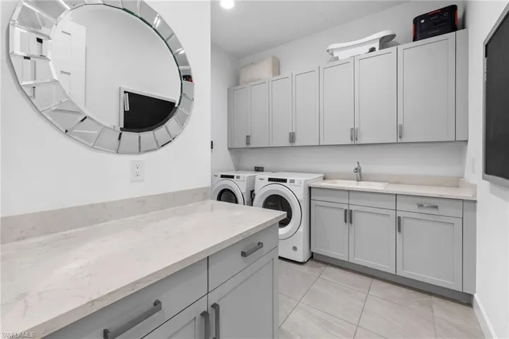 Laundry area featuring tons of storage, washing machine and dryer, sink, and neutral tile flooring