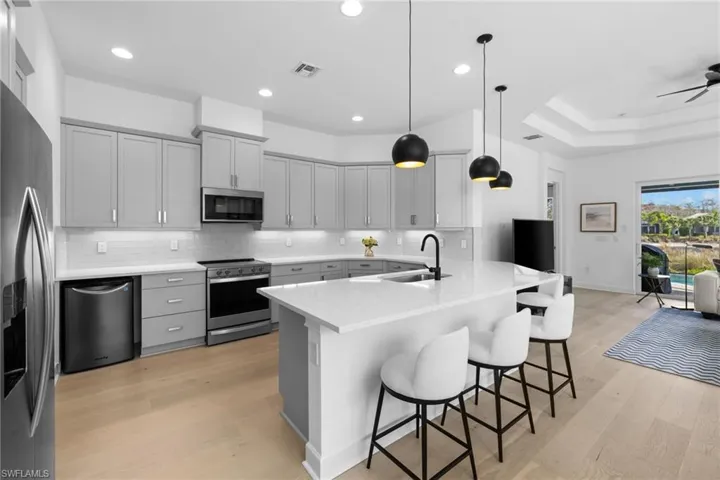 Kitchen featuring gray cabinetry, a kitchen bar, stainless steel appliances, a peninsula, and light wood finished floors