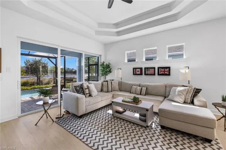 Living area featuring a sunroom, light wood-style flooring, ceiling fan, a tray ceiling, and a water view
