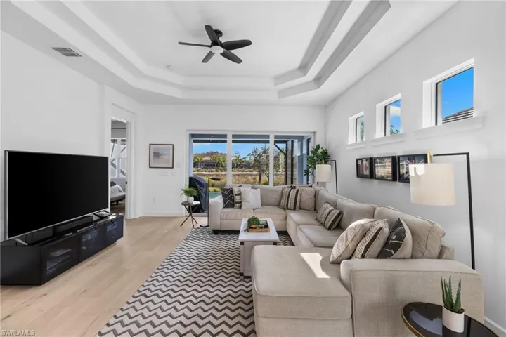 Living area featuring a ceiling fan, light wood finished floors, and a raised ceiling