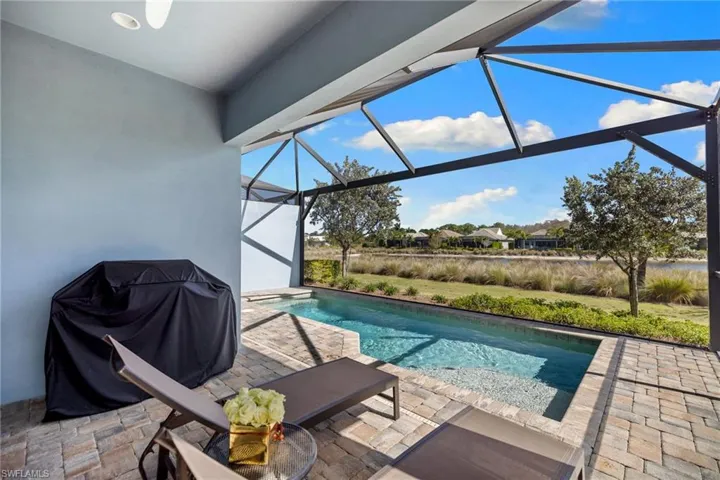 Swimming pool with glass enclosure, a grill, a sunroom, a patio area, and a residential view