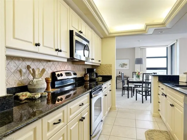 Kitchen featuring stainless steel appliances, dark stone countertops, crown molding, a tray ceiling, and light tile patterned floors