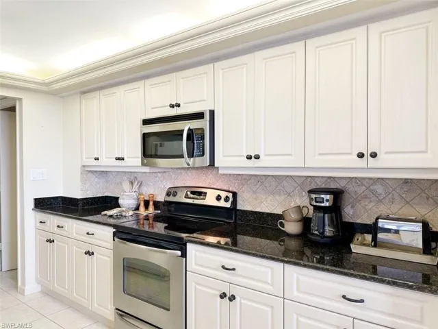 Kitchen featuring stainless steel appliances, white cabinetry, dark stone countertops, tasteful backsplash, and ornamental molding