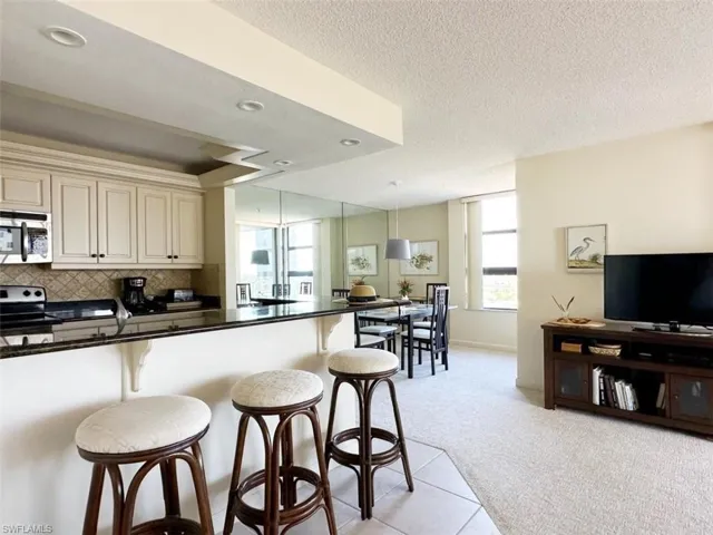 Kitchen featuring cream cabinets, a breakfast bar area, stainless steel appliances, light colored carpet, and a textured ceiling