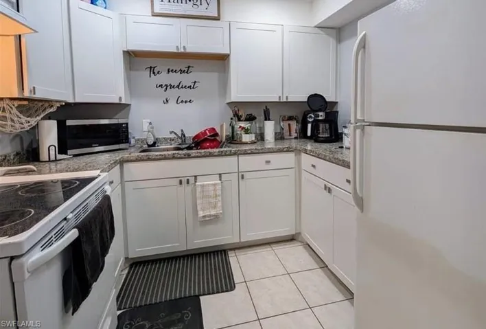 Kitchen featuring light tile patterned floors, white appliances, sink, white cabinetry, and stone countertops