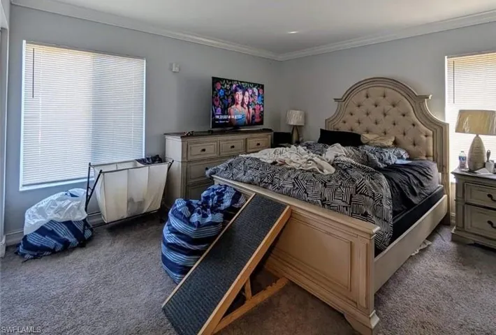 Bedroom with ornamental molding and dark colored carpet