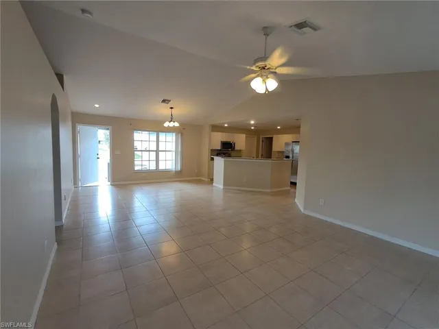 Unfurnished living room with light tile patterned flooring, lofted ceiling, hanging lights, and a ceiling fan