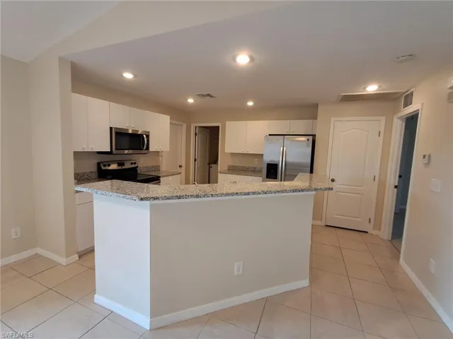 Kitchen with white cabinets, light stone counters, stainless steel appliances, a kitchen island, and light tile patterned flooring