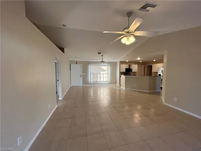 Unfurnished living room with a ceiling fan, light tile patterned floors, vaulted ceiling, and arched walkways