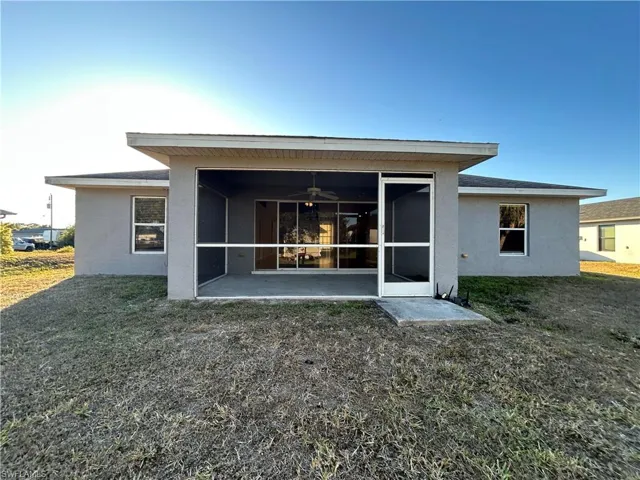 Rear view of house featuring a sunroom, stucco siding, a lawn, and a ceiling fan