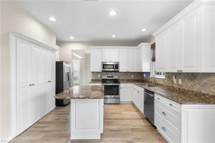 Kitchen with white cabinets, appliances with stainless steel finishes, dark stone countertops, light wood finished floors, and backsplash