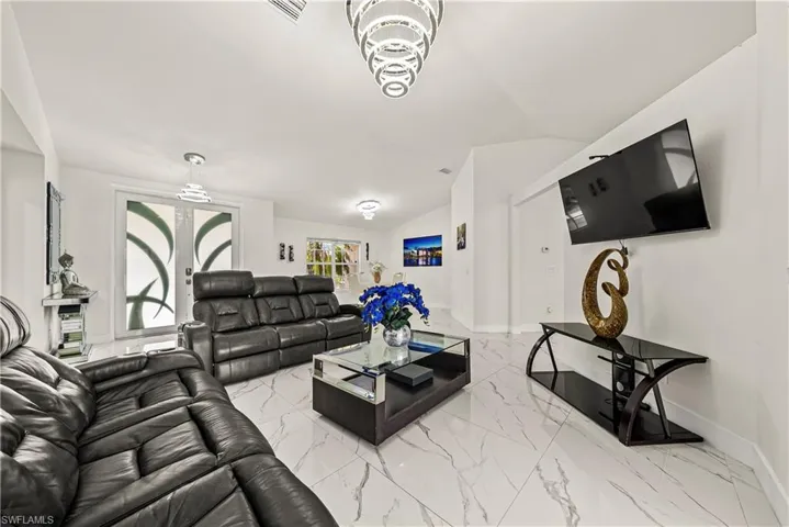 Living area with vaulted ceiling, light marble finish flooring, and hanging lights
