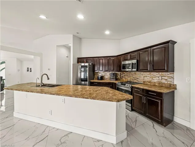 Kitchen with vaulted ceiling, stainless steel appliances, dark wood finish cabinetry, a spacious island, and tasteful backsplash